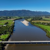 Aerial view of a road bridge crossing a broad river, looking upriver towards mountains